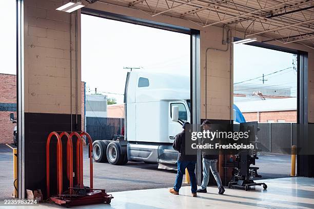 workers inspecting semi-truck in garage for service maintenance - vrachtwagentransport stockfoto's en -beelden