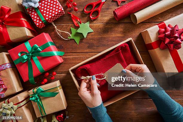 high angle view of woman wrapping christmas present on rustic wooden table - avvolto foto e immagini stock