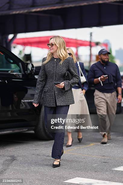 Guest wears blonde shoulder-length wavy hair with a center part, tortoiseshell sunglasses, black leather clutch bag, a grey tweed collarless coat...