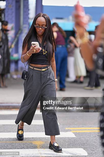 Guest wears long straight black hair with center part, small rectangular tortoiseshell sunglasses, a gold triangular pendant necklace, a thin gold...