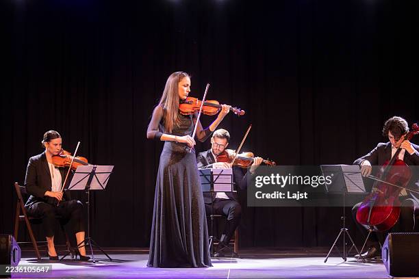 graceful violinist performs with string quartet on elegant stage in dramatic lighting - klassiek-concert stockfoto's en -beelden