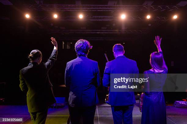 backstage view of musicians waving to audience under stage lights - performer stock pictures, royalty-free photos & images