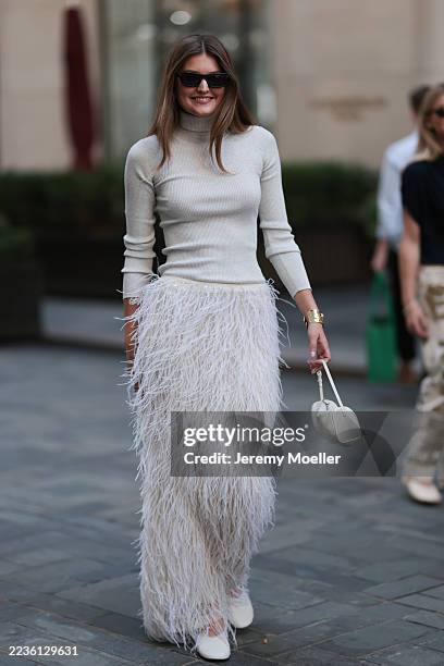 Guest with brown hair worn down is seen wearing a long white fringed skirt, a white turtleneck sweater, white ballerina shoes, a white leather...