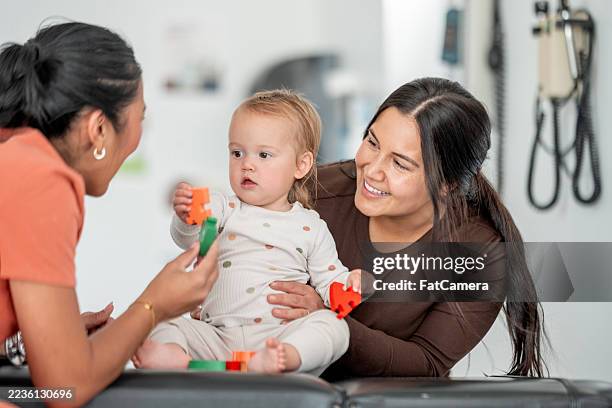 loving interaction between diverse women and baby at a health checkup - foster care stock pictures, royalty-free photos & images