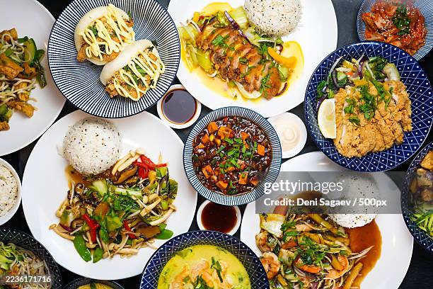 a vibrant overhead shot showcasing a variety of delicious asian dishes, including bao buns, rice, and stir-fries, arranged on a dark table - asiatische küche stock-fotos und bilder