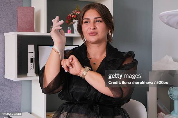 woman wearing a black sheer top and gold watch, putting on a clear glove, in what appears to be a beauty salon or clinic setting - putting book on shelf stock pictures, royalty-free photos & images