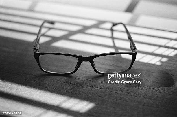 pair of eyeglasses on desk next to window - gafas de leer fotografías e imágenes de stock