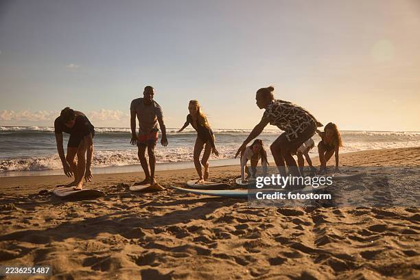group learning surfing techniques on the beach under a clear sky - surf school stock pictures, royalty-free photos & images