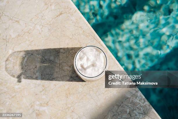 a top view of a layered iced coffee with a frothy top, set on a marble surface beside a shimmering swimming pool. - schwimmbeckenrand stock-fotos und bilder