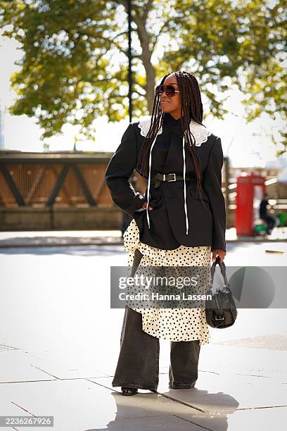 Guest wearing sunglasses, black blazer with black belt, white lace collar, white polka dot midi skirt, black washed jeans and black bag outside...