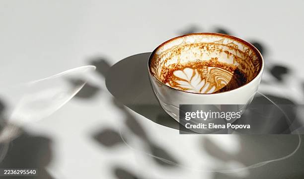 half full latte art cappuccino against ambient lights and shadows background in the local sidewalk cafe - half full stock pictures, royalty-free photos & images