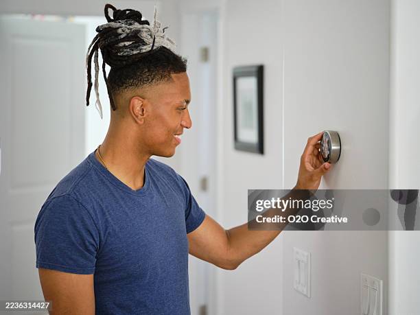 young man adjusting a smarthome thermostat - smart thermostat stock pictures, royalty-free photos & images