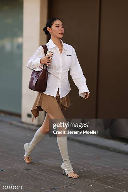 Guest seen wearing a crisp white cotton button-down shirt by Ann Andelman, styled effortlessly with the hem loosely tucked, a camel-brown...