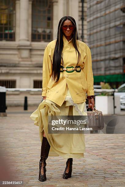 Guest wearing yellow leather jacket with green belt, yellow skirt, lace up boots and a dark beige bag outside TOGA during London Fashion Week on...
