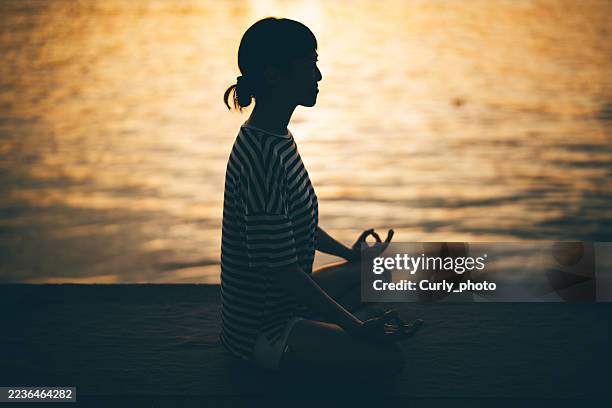 asian woman meditates while doing yoga near the water. - sich verschönern stock-fotos und bilder