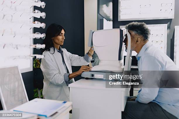 female ophthalmologist performing eye examination on senior male patient using diagnostic equipment at a modern eye clinic. - astigmatism stock pictures, royalty-free photos & images
