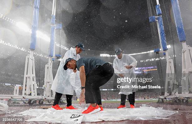 Officials are seen covering the cage floor during heavy rainfall ahead of the Men's Discus Throw Final on day nine of the World Athletics...