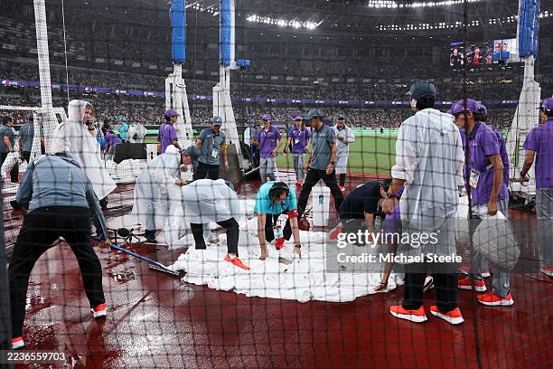 Officials and ground staff are seen working on the cage floor following heavy rainfall ahead of the Men's Discus Throw Final on day nine of the World...
