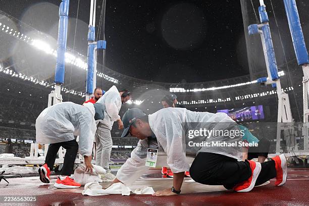 Officials and ground staff are seen covering the cage floor during heavy rainfall ahead of the Men's Discus Throw Final on day nine of the World...