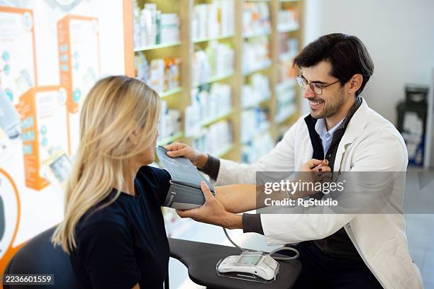 pharmacist checking woman's blood pressure in pharmacy - preventive care stock pictures, royalty-free photos & images