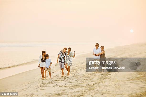 wide shot multigenerational family enjoying walk on beach at sunset - plano geral imagens e fotografias de stock
