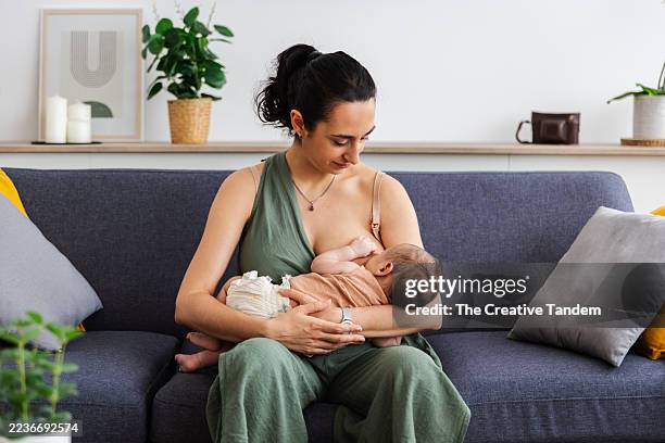 mother breastfeeding newborn baby on living room couch - breastfeeding stock pictures, royalty-free photos & images