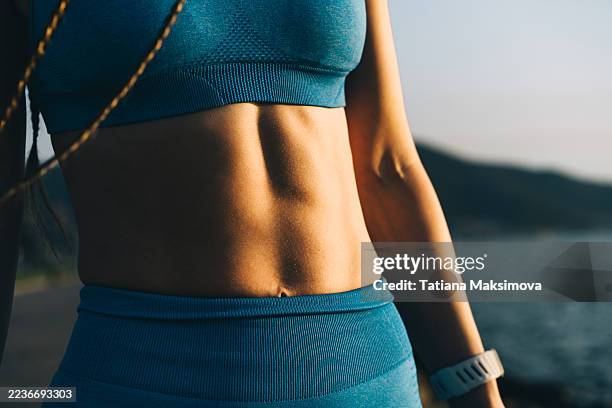 a close-up of a woman's athletic torso, showing her toned abs and a blue sports bra. - torso stock pictures, royalty-free photos & images