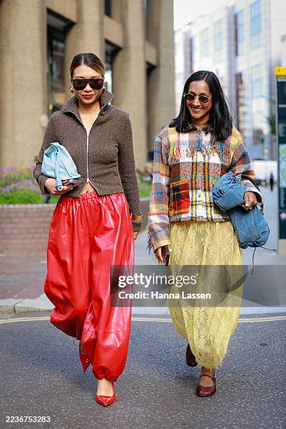 Guest wearing oversized sunglasses, brown zip up cardigan, red balloon pants, red heels and light blue clutch and a guest wearing brown and yellow...