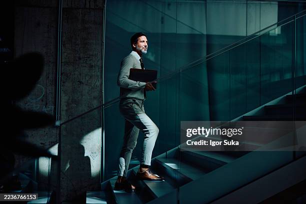 mid adult businessman walking upstairs with determination in modern office - trap stockfoto's en -beelden