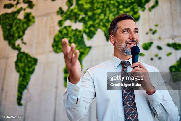 mid adult businessman giving presentation on sustainability in front of world map - voice stock pictures, royalty-free photos & images