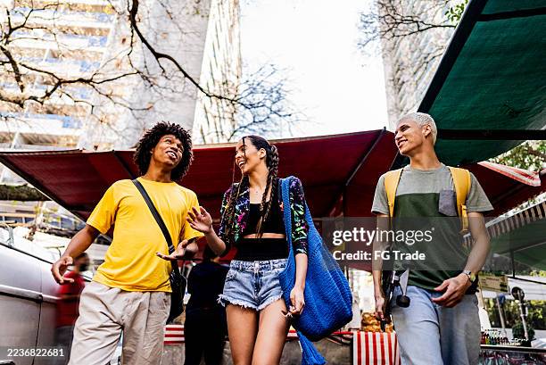 young friends talking while walking at a street market - skateboard shop stock pictures, royalty-free photos & images