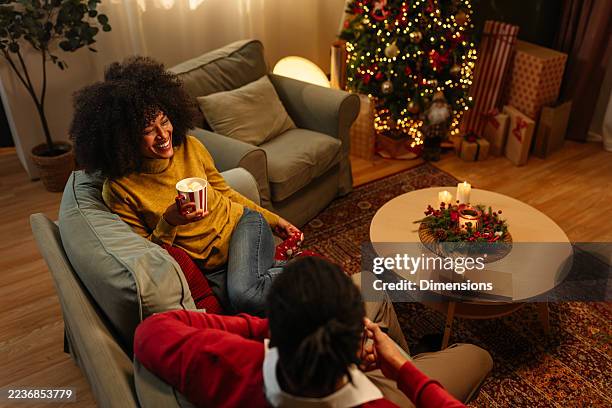 couple relaxing on sofa, drinking hot chocolate and enjoying christmas night at home - cosy christmas stock pictures, royalty-free photos & images