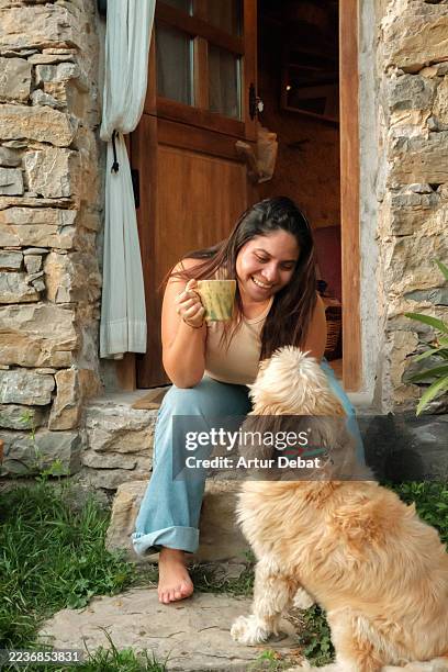 joyful woman enjoying coffee and bonding with her dog at rustic countryside home - zuid europese etniciteit stockfoto's en -beelden