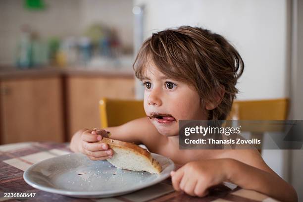 cute boy enjoying bread with chocolate spread at home kitchen table - chocolate bread stock pictures, royalty-free photos & images
