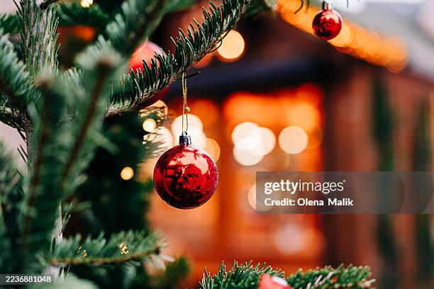 red christmas ornament hanging on pine branch with warm holiday lights in background - charmant stock-fotos und bilder