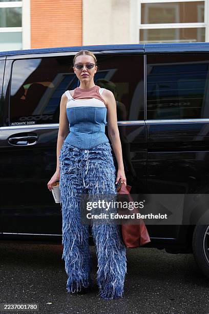 Guest wears hair slicked back into a low bun, small rectangular mirrored sunglasses with thin silver frames, a slouchy brown / burgundy fold-over...