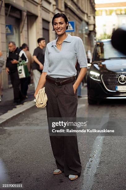 Guest wears a light blue knit polo top tucked into high-waisted brown wide-leg trousers with a leather belt, paired with two-tone flats, a cream...