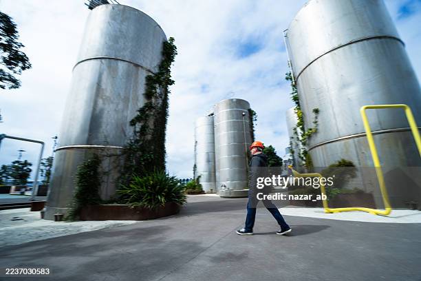 worker walking through industrial plant, inspecting large storage tanks. - silo stock pictures, royalty-free photos & images