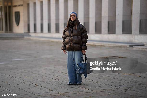 Evi Wave is seen wearing a dark brown high-shine puffer jacket, oversized and voluminous with a high neckline from Oval Square; light blue wide-leg...