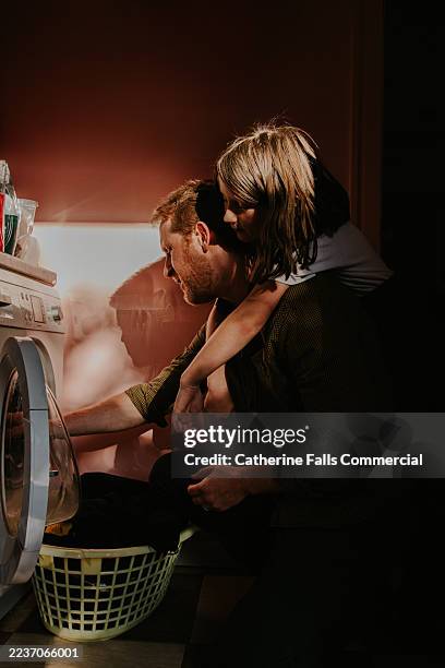father and daughter doing laundry together - his daughter lovingly drapes her arms around his shoulders as he loads the washing machine. - waslijn stockfoto's en -beelden