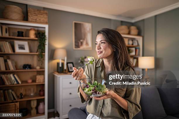 mujer joven disfrutando de una ensalada saludable en su sala de estar - ensalada verde fotografías e imágenes de stock