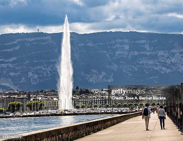 people strolling along the shore of lake geneva ( leman lake) in the afternoon, with its 140-meter-high jet stream. - fountain stock pictures, royalty-free photos & images
