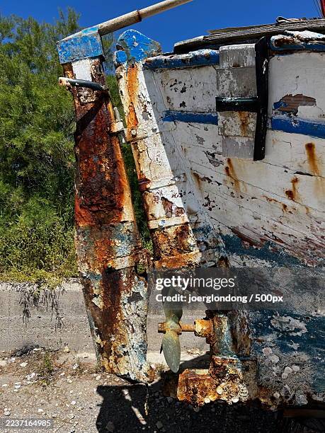 close-up of a rustic, weathered boat with peeling paint and heavy rust, revealing a propeller and surrounded by green foliage under a clear blue sky - schiffsschraube stock-fotos und bilder