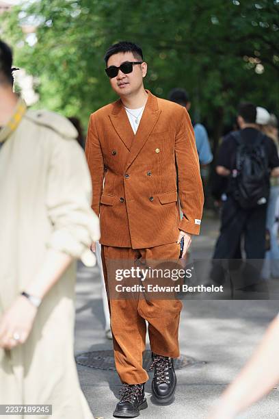 Guest wears short black cropped hair, black rectangular sunglasses, layered silver necklaces with a small pendant, a rust brown corduroy...