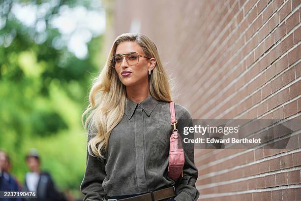 Emili Sindlev wears long blonde wavy hair with a center part, brown-tinted aviator sunglasses with thin gold frames, gold hoop earrings, a pink...