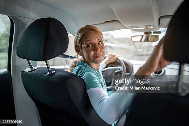 donna conducente che guarda indietro mentre fa retromarcia con l'auto - parcheggiare foto e immagini stock