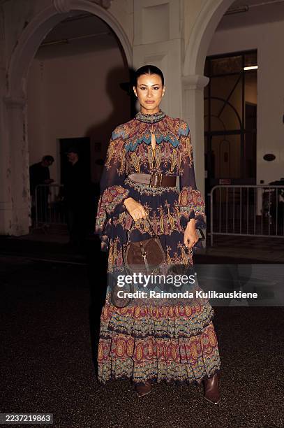 Guest wears a paisley print maxi dress with flared sleeves and a wide brown belt and carries a brown suede handbag and brown boots outside Etro show...