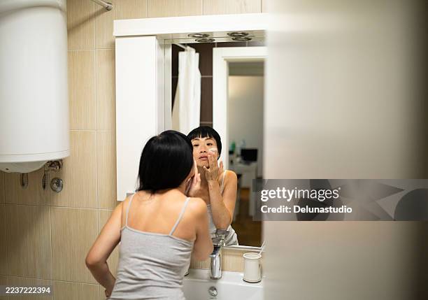 woman applying face cream in bathroom mirror - stock photo - vanity mirror stock pictures, royalty-free photos & images