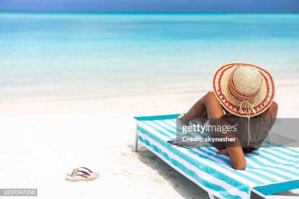back view of a woman relaxing on a deck chair at the beach. - beach holiday stock pictures, royalty-free photos & images