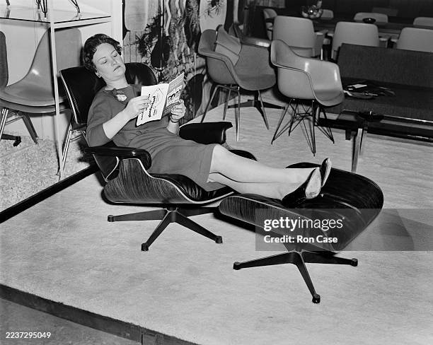 Woman seated in a lounge chair and ottoman by American designer Charles Eames at a press preview of the Furniture Exhibition in Earl's Court, London,...